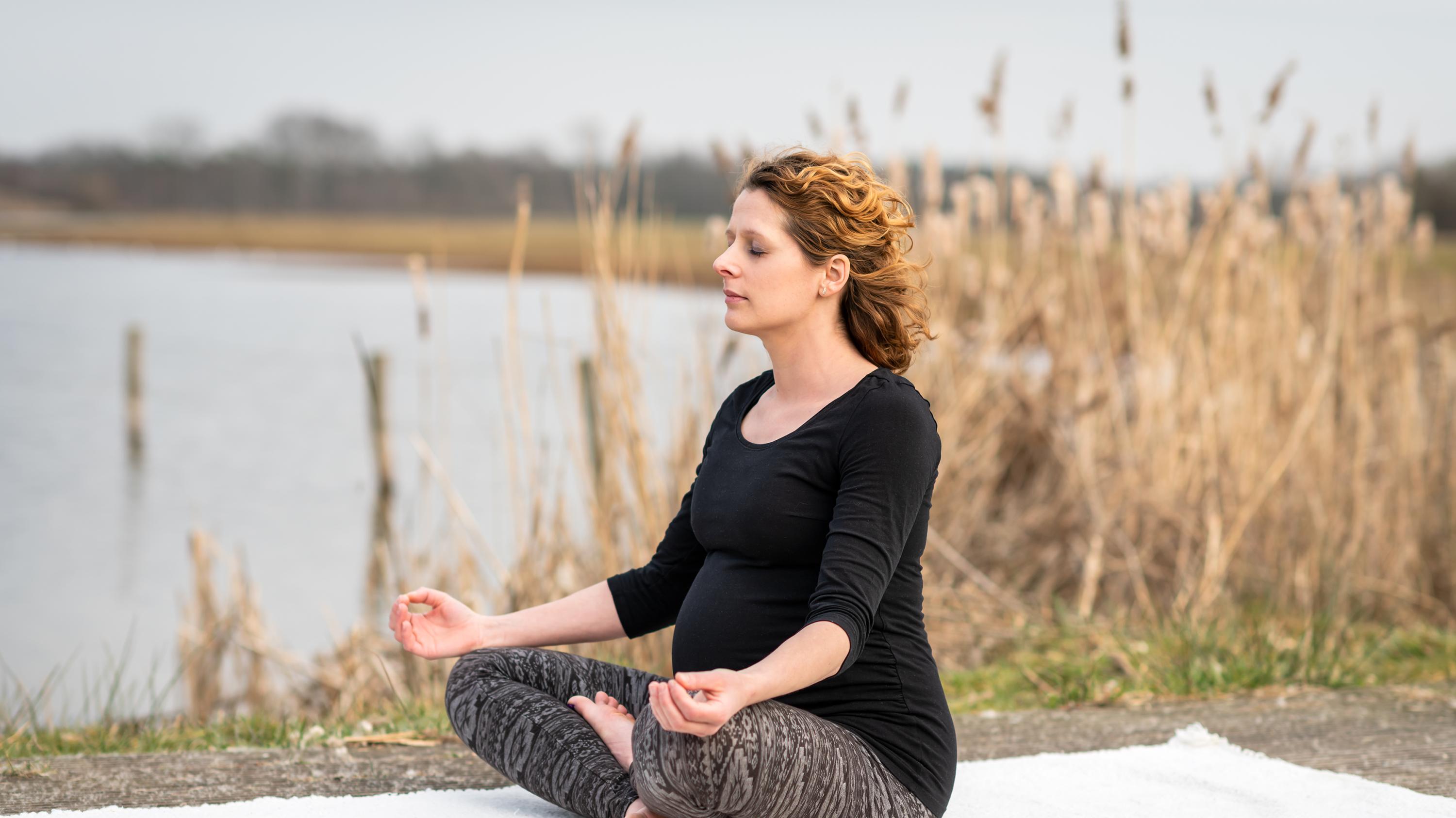 zwangere vrouw mediteert buiten bij het water