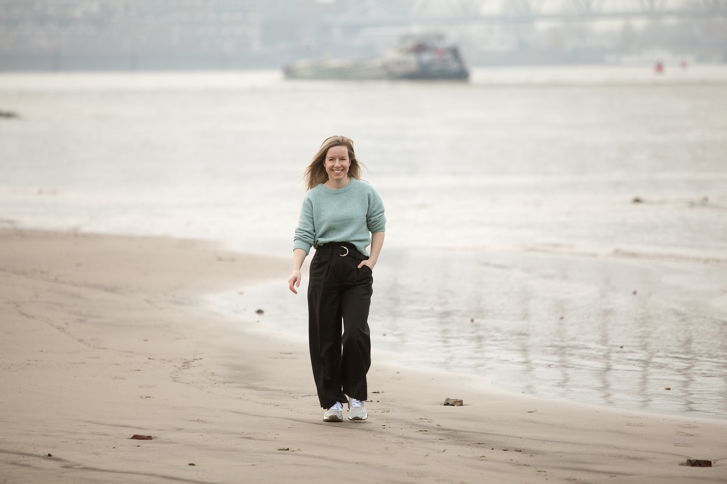 Vrouw lopend over het strand met schip op achtergrond