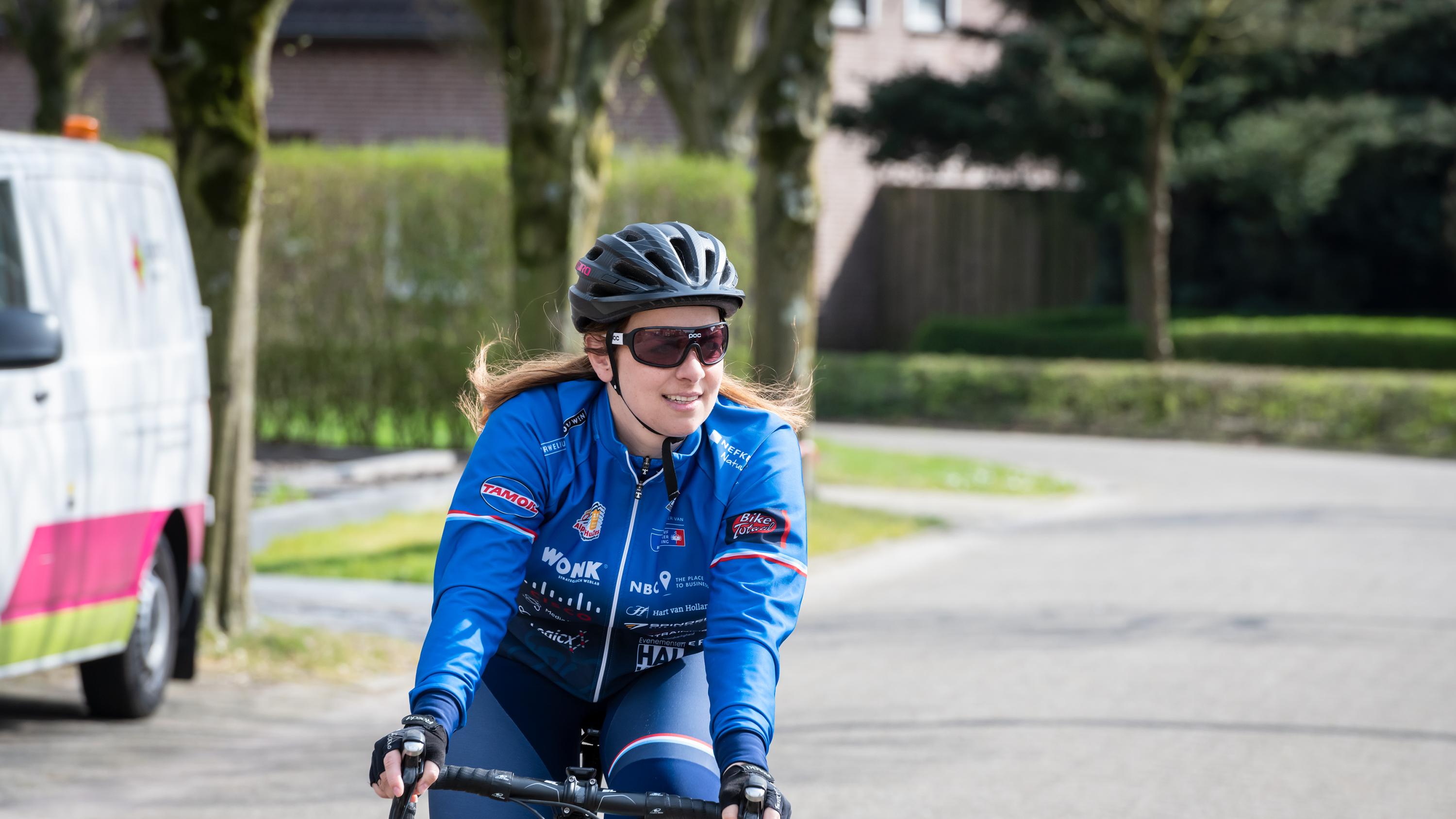 vrouw met helm en blauwe jas op een racefiets